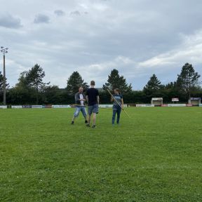 Drei Menschen auf einem Fußballfeld, zwei tragen einen Langstock, eine erklärt.