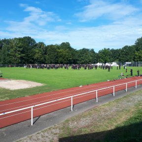 Große Gruppe Hapkidos trainiert auf einem Sportplatz. Im Vordergrund eine Tartan-Bahn, im Hintergrund ein Wald.