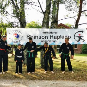 Eine Gruppe in schwarzen Shinson-Hapkido-Anzügen positioniert sich unter einem Shinson-Hapkido-Banner.